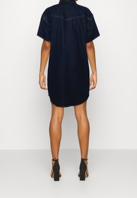 Denimklänning i mörkblått, kortärmad, med rundad nederkant och krage. Har sömnadsdetaljer och en avslappnad passform.