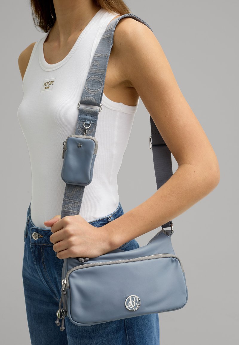 La borsa a tracolla grigia presenta un materiale liscio, hardware in argento, una tasca con zip e una tracolla regolabile a fantasia.