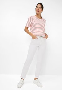 Gestreept T-shirt in het wit met rode lijnen, gecombineerd met witte broek en witte sneakers. De outfit heeft een eenvoudig ontwerp en een losse pasvorm.