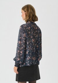 Bluză florală în navy închis, dintr-un material transparent cu textură moale, având mici flori roz și albe, mâneci lungi și mansete cu pliuri.