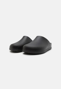 Zoccoli neri con una superficie liscia e opaca; forma arrotondata; design aperto sul retro; suola resistente per comfort e aderenza; dettaglio logo discreto.
