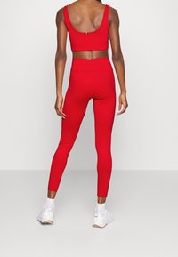 Top corto sportivo rosso e leggings a vita alta realizzati in un tessuto liscio e elastico. Caratterizzato da un design aerodinamico con dettagli minimalisti.