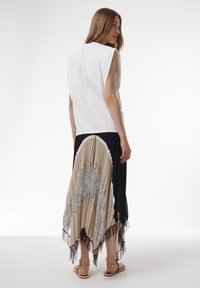 Top blanco sin mangas combinado con una falda plisada en colores beige y negro, con intrincados detalles de encaje y un dobladillo en capas.