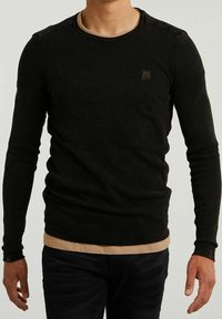 Czarna, długorękawowa koszulka termiczna o teksturowanej powierzchni, okrągłym dekolcie i małym logo na piersi. Nałożona na jaśniejszą podkoszulkę.