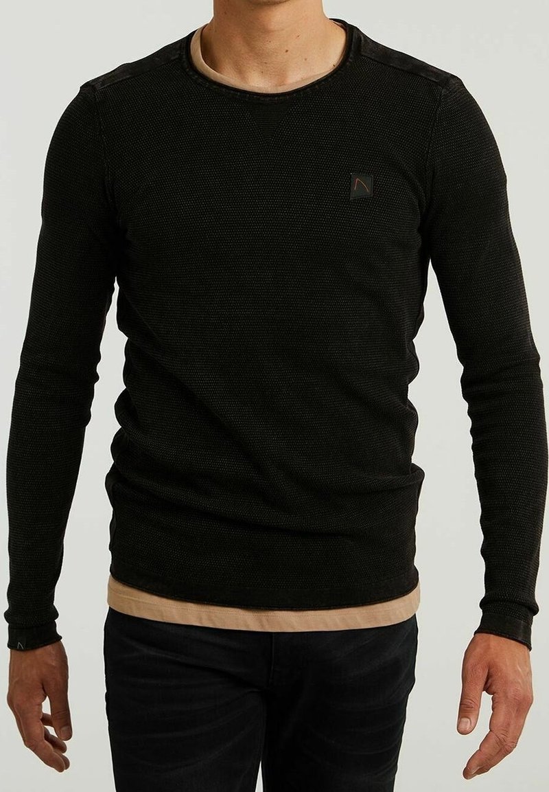 Czarna, długorękawowa koszulka termiczna o teksturowanej powierzchni, okrągłym dekolcie i małym logo na piersi. Nałożona na jaśniejszą podkoszulkę.