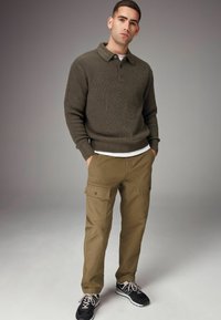 Mørkegrøn ribbet sweater med krave, parret med beige cargo bukser med side lommer. Sorte sneakers fuldender outfitet.