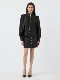 Black textured blouse and skirt set with a high collar, long puffed sleeves, and gold buttons down the front. Black heels complete the look.
