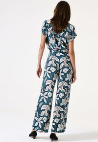 Blumenoverall in Blau mit weißen und roten Mustern, mit weitem Bein und rüschigem Ausschnitt. Hergestellt aus leichtem Stoff.
