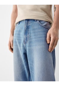 Ljusblå denimjeans med en avslappnad passform, som har synliga sömmar, framfickor och en något urtvättad yta. Midjan är utan dekorationer.