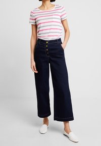 Camiseta de algodón a rayas en gris, rosa y blanco, con un bolsillo; combinada con pantalones de mezclilla de pierna ancha en azul oscuro con cierre de botón y detalles de costura.