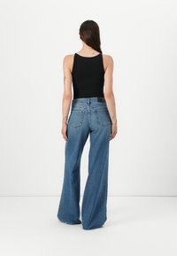 Jeans in denim blu a gamba larga con vita alta, caratterizzati da un classico design a cinque tasche e dettagli di cucitura, abbinati a un top aderente nero.