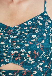 Blommönstrad tealtyg med rynkat halslinning, med ett utskuret detalj. Små blommor i rosa, vitt och lila toner. Justerbara axelband.