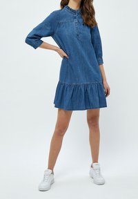 Denim dress with a collared neckline, ruffled trim, three-quarter sleeves, and a tiered skirt. Worn with white sneakers.