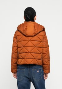 Brun quiltet puffjakke med hætte, prydet med et diamantmønster. Kombineret med blå jeans, som har et cropped design i taljen.