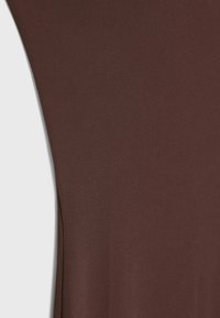 Zbliżenie na gładki, ciemnobrązowy materiał z zaokrąglonym szwem po lewej stronie na jasnym tle.