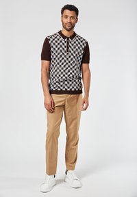 Brown and patterned short-sleeve polo shirt with a knitted design, paired with tan trousers and white sneakers.