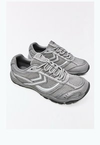 Paire de baskets de sport grises en tissu mesh, design lacets et semelles en caoutchouc sur fond blanc.