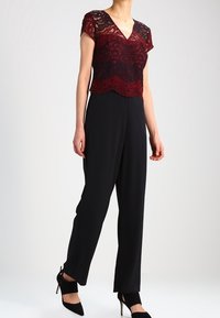 Lace top in bordeaux en zwart met korte mouwen, gelaagd ontwerp. Zwarte wijde broek, gladde stof, gecombineerd met zwarte hoge hakken.