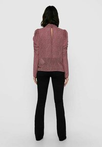 Rød blomstret bluse med puffede ærmer, høj krave og en nøglehul-detail bagpå, parret med sorte flared bukser. Simpelt, struktureret stof.