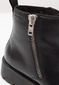 Bottines noires en cuir avec une fermeture éclair argentée, une semelle solide et des détails cousus. Le design est élégant avec une finition mate.