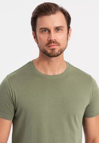 T-shirt verde oliva a maniche corte realizzato in cotone morbido. Presenta un collo rotondo e una vestibilità rilassata, con dettagli di cucitura visibili all'orlo.
