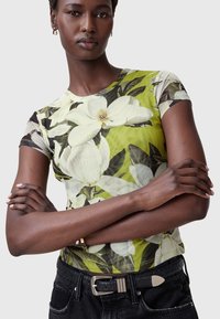 Blomsterkortærmet t-shirt i grøn og hvid, der har et blødt stof, rund halsudskæring og detaljeret magnolia tryk, parret med sorte jeans.