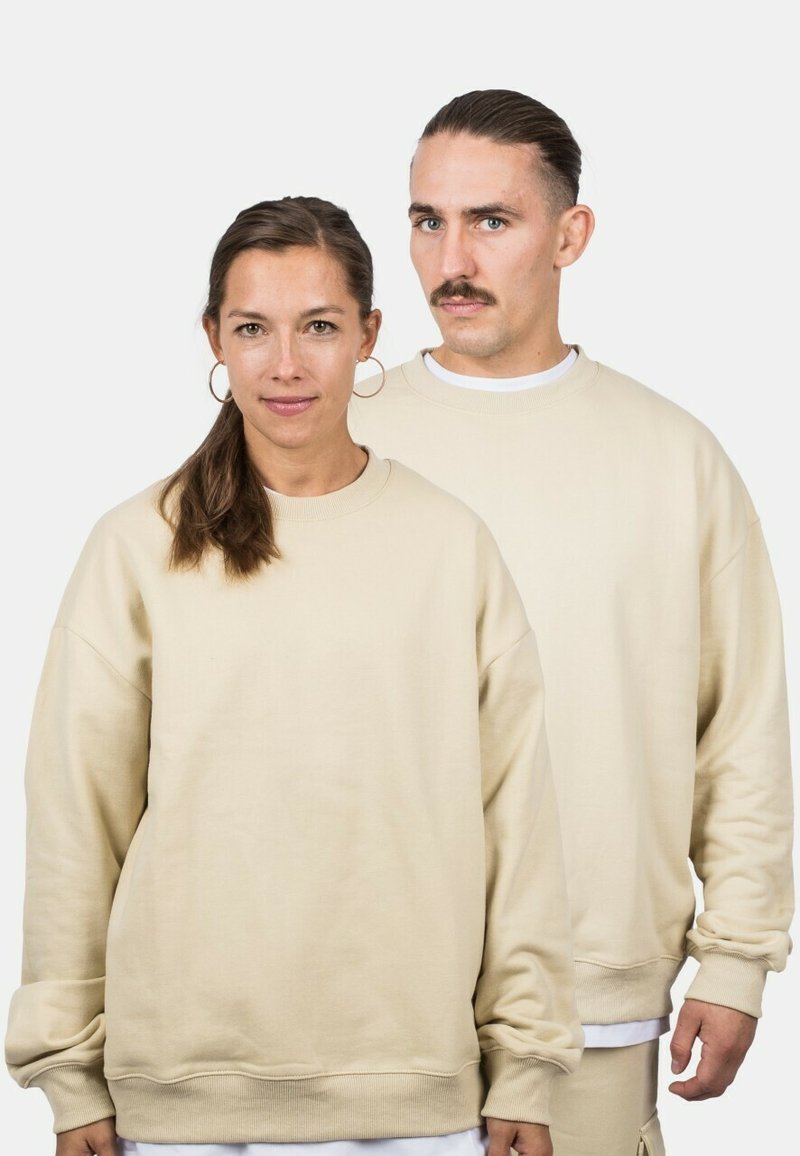 Felpe beige con un taglio rilassato, dotate di polsini a coste e colletto girocollo. Il tessuto appare morbido e testurizzato, adatto per l'abbigliamento casual.