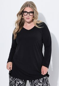 Schwarzes Langarm-V-Ausschnitt-Shirt aus weichem Stoff, kombiniert mit gemusterten Schwarz-Weiß-Leggings mit floralen Motiven.