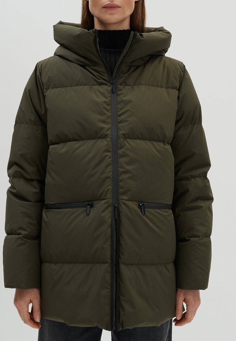 Olivgrüne gepolsterte Pufferjacke mit Reißverschluss vorne, verstellbare Kapuze, zwei mit Reißverschluss gesicherte Taschen und einem gesteppten Design. Schwarze Akzente an den Reißverschlüssen.