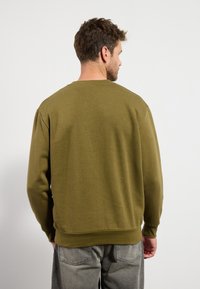 Oliwkowy sweatshirt z okrągłym dekoltem, ściśniętymi mankietami i dołem. Miękka tekstura, swobodny krój i lekko oversize; brak widocznych wzorów.