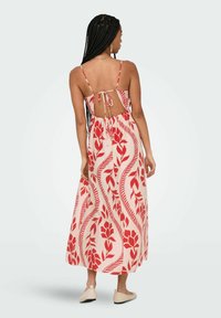 Robe maxi en tissu rose clair avec des motifs floraux rouges. Bretelles spaghetti, dos ouvert avec fermeture à nouer, taille élastique et jupe fluide.