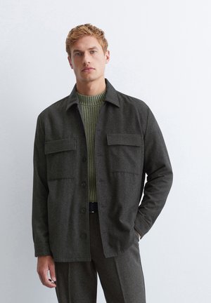 Dark gray wool jacket with a button front, two chest pockets, and a collar, layered over a textured green sweater. Smooth, tailored fit.
