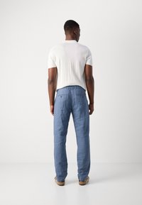 Pantaloni din in de culoare albastru deschis, cu o croială confortabilă, având două buzunare la spate și un brâu cu urechi pentru curea, purtați cu o cămașă albă cu mânecă scurtă.