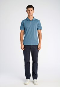 Jasnoniebieska koszulka polo z klasycznym kołnierzykiem i białym wykończeniem, zestawiona z ciemnogranatowymi spodniami i białymi tenisówkami. Dopasowany krój i teksturowana tkanina.