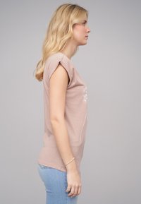 Lyserød t-shirt med korte ærmer lavet af blødt stof, med et mælkebøtteprint på forsiden, parret med bla jeans.