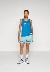 Turquoise tank top with "FLY" print and gray swim shorts featuring a diamond pattern and blue stripes. Black and white athletic shoes.