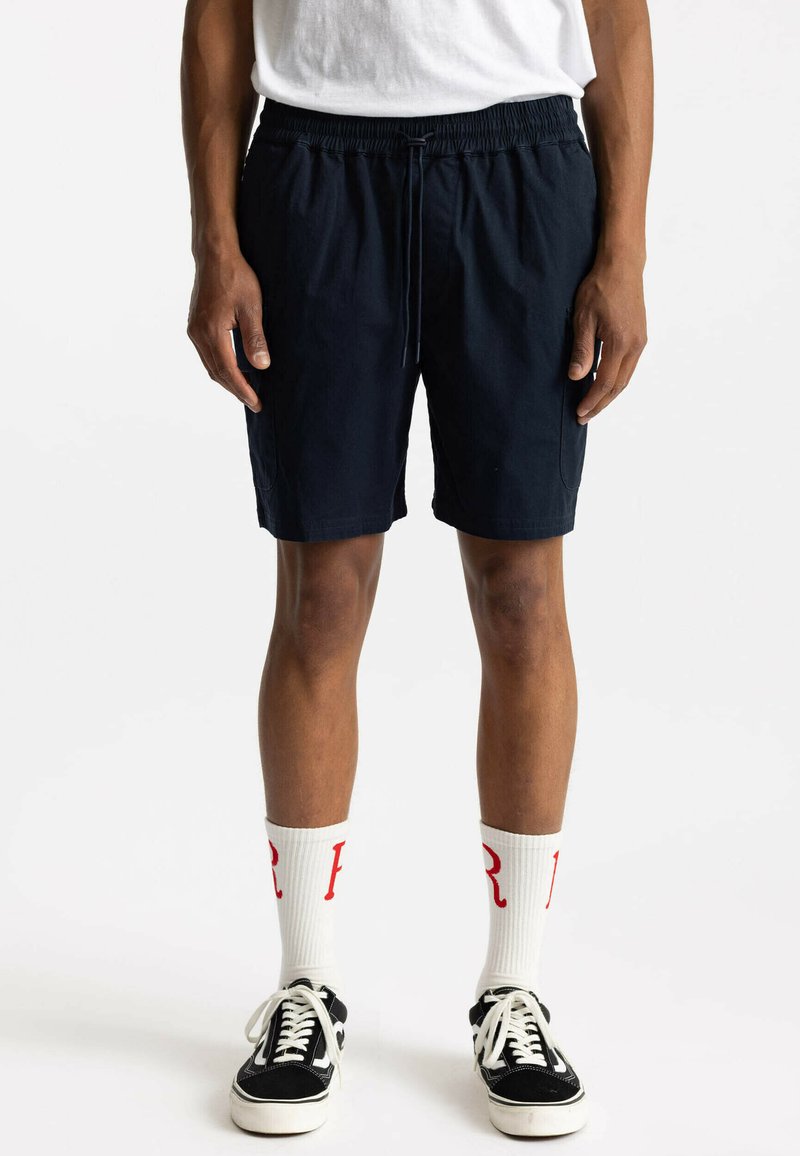 Marineblauwe shorts met elastische tailleband en een trekkoord, met twee zijzakken, gecombineerd met witte sokken en zwarte sneakers.