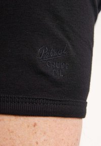 Tricou din bumbac negru, cu textură ribbed, mâneci scurte și un logo brodat subtil pe tiv, realizat din fir negru.
