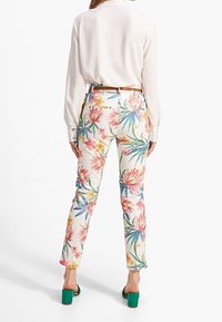 Bloemige broeken met een witte achtergrond, versierd met roze en gele bloemen en groene bladeren. Strak model met achterzakken.