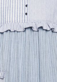 Blå och vit vertikalt randig klädsel med veckad midja och volangdetaljer, med små svarta knappar på den övre delen.