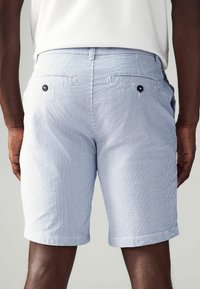 Bermudas para hombre en azul claro con un patrón de rayas blancas. Cuenta con dos bolsillos traseros con cierres de botón. Confeccionadas en una mezcla de algodón texturizado.