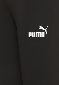 Leggings neri in cotone con logo Puma bianco e il design del gatto che salta sulla coscia. Texture liscia, design aderente.