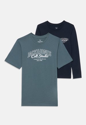 Twee t-shirts: één in teal, met korte mouwen en een wit logo, en één in marineblauw, met lange mouwen en een klein wit logo op de borst.