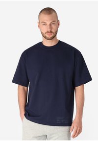 Navy cotton t-shirt with a round neck, short sleeves, and a relaxed fit. Features subtle text detail at the hem. Smooth texture.