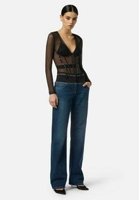 Top nero a maniche lunghe in mesh con profonda scollatura a V, sovrapposto a un reggiseno nero, abbinato a jeans a gamba larga blu scuro a vita alta.