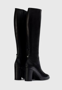 Botas altas de cuero negro hasta la rodilla con un grueso tacón alto, que cuentan con una cremallera en la parte trasera y un sutil detalle de marca en el tacón.