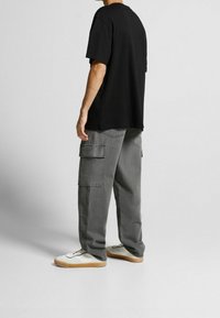 Černé oversized tričko zkombinované se šedými cargo kalhotami s mnoha kapsami. Celý outfit doplňují bílé tenisky s gumovou podrážkou.