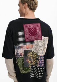 Černé triko s různými patchworkovými designy, včetně kostkovaného, bandana a leopardího potisku s odlišnými texturami a barvami.