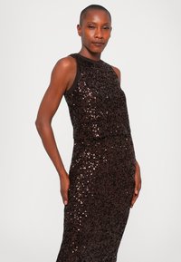 Abito arricchito di paillettes in marrone scuro. Design semplice e aderente con un collo alto e silhouette senza maniche. Texture liscia e lucentezza sottile.