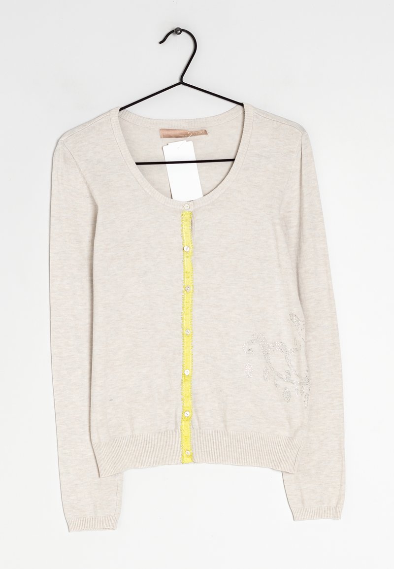 Ljusbeige cardigan med rund hals, gul knappslå, ribbstickade muddar och fåll samt dekorativa silverdetaljer på ena sidan.